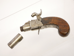 A lovely early 19th-century English 40-bore boxlock percussion muff pistol by Henry Nock of London, converted from flintlock and with the original sliding safety catch removed. It features a 1.5-inch turn-off barrel bearing Birmingham proof marks, while the action is finely engraved with war trophies and signed “H. Nock, London.”