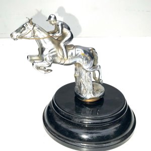 A super bronze jumping horse & rider car mascot. Made from chromed bronze, in the form of a horse & rider jumping a fence, this mascot has been mounted on a black marble base early 20th century, makers name on horses flank, conditions used showing some blemishes, placed on black base for display looks inspiring, standing 18 cm high to include base, length of 14 cm bases diameter 16 cm.