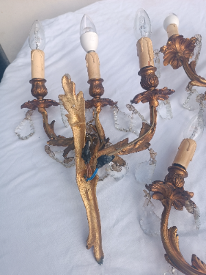 A set of three rococo revival wall sconces in gilt metal, with foliage shaped wall mounts and arms, and foliate drip trays from which leaf shaped cut glass drops hang. 
Two wall sconces with triple arms and the other with twin arms.
Size approx 48 cm high x 32 cm wide for the sconce with three arms.