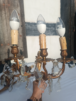 A set of three rococo revival wall sconces in gilt metal, with foliage shaped wall mounts and arms, and foliate drip trays from which leaf shaped cut glass drops hang. 
Two wall sconces with triple arms and the other with twin arms.
Size approx 48 cm high x 32 cm wide for the sconce with three arms.