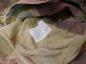 An original British Airborne Denison Smock dating from the post-1946 period. Commonly referred to as the Third Pattern or 1946 Pattern, this version retained many of the features of the wartime Second Pattern smock and remained in service with British and Commonwealth airborne forces for many years. The Denison Smock continued as standard combat clothing for the Royal Marines and the Parachute Regiment until the mid-1970s.

This example displays the distinctive screen-printed camouflage pattern, featuring a light sand-coloured base overlaid with broad green and reddish-brown brushstrokes. Characteristic post-war features include knitted cuffs, nickel-plated Newey press studs, a brass Swift half-zip with its original pendant pull, shoulder epaulettes, a wool-lined collar, and the distinctive rear fishtail, which fastens to the front using the original press studs.

The original internal label is still present, although it has faded through laundering and is no longer legible.

Presented in good overall condition, the smock exhibits honest service wear consistent with its age. It retains its original knitted cuffs and remains complete throughout, making it an excellent example with strong display appeal as well as being perfectly wearable.