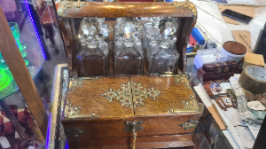 A Victorian oak tantalus, the three decanters restrained within a mirrored niche, hinged twin-covers enclosing provision for cigars and playing-cards, drawer to base, carrying handles to sides, applied with Gothic brass cut-card work. Centre decanter has a single chip on the neck.

Size: 33cm high, 37cm wide.