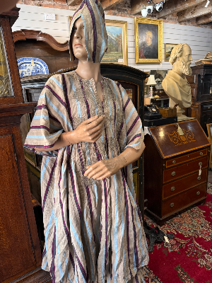 A striking mid-20th-century West African ceremonial ensemble, traditionally attributed to the Yoruba, comprising a voluminous agbada outer gown, ṣòkòtò trousers and fìlà cap.

The agbada is constructed from narrow strips of handwoven cloth in a natural cream ground, patterned with alternating blue and burgundy stripes. The front is extensively decorated with elaborate hand-worked embroidery, including large interlocking and quatrefoil motifs arranged symmetrically across the body of the gown.

Previous owner said he brought it back from West Africa in 1954 and identified it as belonging to the Yoruba.

Date: Mid-20th century, associated label dated 1954
Origin: Nigeria / West Africa
Attribution: Yoruba
Materials: Handwoven textile, embroidered decoration

Condition: Vintage condition consistent with age and traditional use. Please refer to photographs for individual areas of wear, marks, repairs or losses.