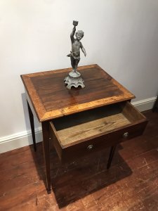 Elegant period antique Sheraton-style side table, circa 1780, featuring a satinwood cross-banded top and a front drawer with original brass handles. One ring handle is missing due to age. Delicate tapered legs are decorated with string inlay, and the drawer has a pine lining. The table has a faded colour and shows signs of wear consistent with age and use. Dimensions: 31.5 inches high × 23 inches wide × 19 inches deep.