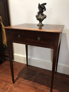 Elegant period antique Sheraton-style side table, circa 1780, featuring a satinwood cross-banded top and a front drawer with original brass handles. One ring handle is missing due to age. Delicate tapered legs are decorated with string inlay, and the drawer has a pine lining. The table has a faded colour and shows signs of wear consistent with age and use. Dimensions: 31.5 inches high × 23 inches wide × 19 inches deep.