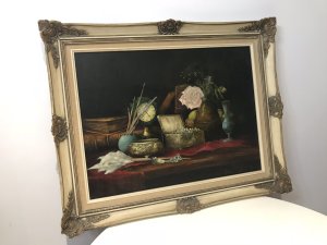 Original vintage still-life oil painting on canvas, signed with the artist’s initials C.M.P. The composition depicts a jewel casket, French clock, leather-bound books, pink rose, artist’s oil paint and brush, and a green glass vase arranged on a table. Vibrant colours and fine detail enrich the scene, presented in an ornate carved giltwood frame. Dimensions: 24 inches high × 30.5 inches wide.