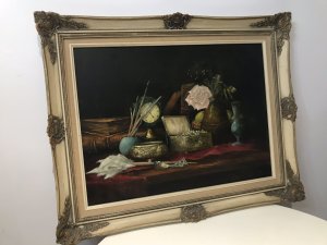 Original vintage still-life oil painting on canvas, signed with the artist’s initials C.M.P. The composition depicts a jewel casket, French clock, leather-bound books, pink rose, artist’s oil paint and brush, and a green glass vase arranged on a table. Vibrant colours and fine detail enrich the scene, presented in an ornate carved giltwood frame. Dimensions: 24 inches high × 30.5 inches wide.