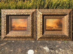Pair of fine art hunting scene paintings by artist Brain Cooke, circa 1900, executed on oak panels with fine colours and detail. Titled 'The Full Cry' and 'The Chase', the scenes depict mounted hunters navigating water and jumping fences, and red-coated riders galloping with beagles in pursuit. Each painting is presented in an elaborate giltwood frame adorned with fruit, acanthus leaves, roses and orchids. Dimensions not provided.