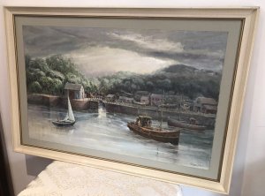 Original oil painting on board depicting a harbour with fishing boats, a canal waterway and houses. Intricate detail and vivid colours capture the waterfront beneath a stormy sky. Signed by Hong Kong-based artist WAN and presented in a cream wooden frame with a painted border.