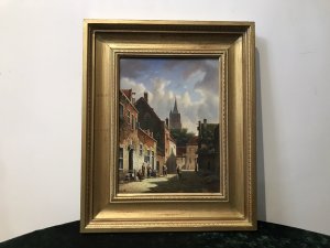 Original Dutch street scene oil painting on board by artist M Ives, presented in a gilt frame. The village view depicts cobbled streets and seven male and female figures in traditional dress, with a spired church in the background beneath a blue sky.