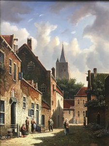 Original Dutch street scene oil painting on board by artist M Ives, presented in a gilt frame. The village view depicts cobbled streets and seven male and female figures in traditional dress, with a spired church in the background beneath a blue sky.