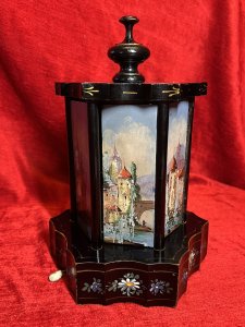 Antique Original Reuge Musical Cigarette Carousel Adorned With Painted Landscape Scenes Circa - Victorian 1890 Composition - Ebony Wood, Mother Of Pearl And Oils Listing Description Fine Quality Swiss Made Musical Cigarette Carousel Constructed In A Hexagonal Form. The Body Is Comprised Of Cylindrical Framework Hanging Six Doors Which Revolve (By Turning The Top Pinnacle CLOCKWISE To Open), Revealing Ornate Brass Individual Cigarette/Cigar Mounts. The Front Of Each Door Decorated With Fine Mother Of Pearl Inlays Intricately Over Painted With Quintessential Costal Town Landscape Scenes And Sailing Boats . Ornamental Scalloped Plinth Base Decorated With Floral Sprays Of Meadow Flowers To Match The Top Of The Carousel. Complete With Original Winding Key For Musical Element Which Plays Beautifully A Array Of Tunes. Video Available Of The Carousel Playing (Please Call If You Require The Video) Winding Keyhole On The Underside. Muiscal Switch On The Side Of The Carousel. Rare & Interesting Collectors Item. Condition - Very Good Antique Signs Of Wear To Paint Work Due To Age And Usage. In Good Working Order. Dimensions In Inches Height 11" Base Diam 7.5" For Further Pictures And Other Information Please Call 07376618513