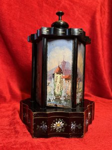Antique Original Reuge Musical Cigarette Carousel Adorned With Painted Landscape Scenes Circa - Victorian 1890 Composition - Ebony Wood, Mother Of Pearl And Oils Listing Description Fine Quality Swiss Made Musical Cigarette Carousel Constructed In A Hexagonal Form. The Body Is Comprised Of Cylindrical Framework Hanging Six Doors Which Revolve (By Turning The Top Pinnacle CLOCKWISE To Open), Revealing Ornate Brass Individual Cigarette/Cigar Mounts. The Front Of Each Door Decorated With Fine Mother Of Pearl Inlays Intricately Over Painted With Quintessential Costal Town Landscape Scenes And Sailing Boats . Ornamental Scalloped Plinth Base Decorated With Floral Sprays Of Meadow Flowers To Match The Top Of The Carousel. Complete With Original Winding Key For Musical Element Which Plays Beautifully A Array Of Tunes. Video Available Of The Carousel Playing (Please Call If You Require The Video) Winding Keyhole On The Underside. Muiscal Switch On The Side Of The Carousel. Rare & Interesting Collectors Item. Condition - Very Good Antique Signs Of Wear To Paint Work Due To Age And Usage. In Good Working Order. Dimensions In Inches Height 11" Base Diam 7.5" For Further Pictures And Other Information Please Call 07376618513
