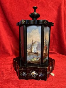 Antique Original Reuge Musical Cigarette Carousel Adorned With Painted Landscape Scenes Circa - Victorian 1890 Composition - Ebony Wood, Mother Of Pearl And Oils Listing Description Fine Quality Swiss Made Musical Cigarette Carousel Constructed In A Hexagonal Form. The Body Is Comprised Of Cylindrical Framework Hanging Six Doors Which Revolve (By Turning The Top Pinnacle CLOCKWISE To Open), Revealing Ornate Brass Individual Cigarette/Cigar Mounts. The Front Of Each Door Decorated With Fine Mother Of Pearl Inlays Intricately Over Painted With Quintessential Costal Town Landscape Scenes And Sailing Boats . Ornamental Scalloped Plinth Base Decorated With Floral Sprays Of Meadow Flowers To Match The Top Of The Carousel. Complete With Original Winding Key For Musical Element Which Plays Beautifully A Array Of Tunes. Video Available Of The Carousel Playing (Please Call If You Require The Video) Winding Keyhole On The Underside. Muiscal Switch On The Side Of The Carousel. Rare & Interesting Collectors Item. Condition - Very Good Antique Signs Of Wear To Paint Work Due To Age And Usage. In Good Working Order. Dimensions In Inches Height 11" Base Diam 7.5" For Further Pictures And Other Information Please Call 07376618513