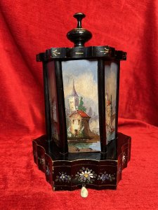 Antique Original Reuge Musical Cigarette Carousel Adorned With Painted Landscape Scenes Circa - Victorian 1890 Composition - Ebony Wood, Mother Of Pearl And Oils Listing Description Fine Quality Swiss Made Musical Cigarette Carousel Constructed In A Hexagonal Form. The Body Is Comprised Of Cylindrical Framework Hanging Six Doors Which Revolve (By Turning The Top Pinnacle CLOCKWISE To Open), Revealing Ornate Brass Individual Cigarette/Cigar Mounts. The Front Of Each Door Decorated With Fine Mother Of Pearl Inlays Intricately Over Painted With Quintessential Costal Town Landscape Scenes And Sailing Boats . Ornamental Scalloped Plinth Base Decorated With Floral Sprays Of Meadow Flowers To Match The Top Of The Carousel. Complete With Original Winding Key For Musical Element Which Plays Beautifully A Array Of Tunes. Video Available Of The Carousel Playing (Please Call If You Require The Video) Winding Keyhole On The Underside. Muiscal Switch On The Side Of The Carousel. Rare & Interesting Collectors Item. Condition - Very Good Antique Signs Of Wear To Paint Work Due To Age And Usage. In Good Working Order. Dimensions In Inches Height 11" Base Diam 7.5" For Further Pictures And Other Information Please Call 07376618513