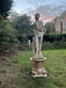 Roman Male Senator 'Augustas' Holding Scripture Set Upon Plinth Garden Showpiece Circa - VintageComposition - Reconstituted Stone Listing Description Standing Male Roman Senator Figure With Left Facing Head, Detailed Facial Features With Mid Length Hair And Headband, Partly Dressed In Draped Loin Cloth Set Over Chest For Modesty. Scripture In Left Hand, Whilst Right Hand Is Placed Upon Tree Stump. Bare Feet In Fine Detail Uponn Rocky Mound. Statue Stands On Circular Gilt Roman Pillar Pedestal. Condition - Excellent Signs Of Weathering To Statue Conducive To Age. Dimensions In Inches Height 40” without plinth Width Depth