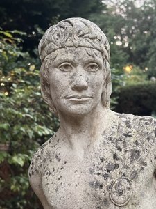 Roman Male Senator 'Augustas' Holding Scripture Set Upon Plinth Garden Showpiece Circa - VintageComposition - Reconstituted Stone Listing Description Standing Male Roman Senator Figure With Left Facing Head, Detailed Facial Features With Mid Length Hair And Headband, Partly Dressed In Draped Loin Cloth Set Over Chest For Modesty. Scripture In Left Hand, Whilst Right Hand Is Placed Upon Tree Stump. Bare Feet In Fine Detail Uponn Rocky Mound. Statue Stands On Circular Gilt Roman Pillar Pedestal. Condition - Excellent Signs Of Weathering To Statue Conducive To Age. Dimensions In Inches Height 40” without plinth Width Depth