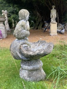 Water Feature Centrepiece Of Faun Boy Sat Upon Scalloped Bowl. Circa - 20th Century Composition- Reconstituted Stone Condition- Weathered Used Pristine Decorative Water Feature Of Scalloped Bowl Set Upon Square Oval Plinth Pediment With Bow And Column Pillared Decoration, With Central Sitting Faun Playing Mouth Organ With Hoove Feet And Bushy Tail. A Hole For Water Hose Through Base Pediment Into Scalloped Bowl. A True Mythological Piece An Asset To Any Garden Decor. Dimensions In Inches Height 30” Width 19” Depth 18” Weight Approx 30Kg Heavy Item