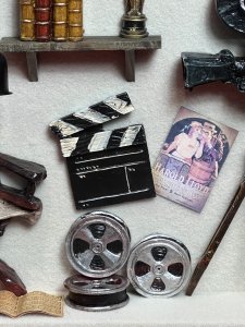 Vintage Diorama Of Film Directors Studio With 1920's Icons Circa - Vintage Composition - Mixed Media Paper/Resin/ Glass/ Wood Listing Description Stylish Diorama Of 1920's Hollywood Directors Studio In Room Of Textured Wallpaper With Wood Exposed Beams, Showcasing Large Camera On Tripod Stand. Wall Shelf With Prevalent Oscar Film Award And Books And Walls Dec0orated With Film Advertisements Including 'Grandma's Boy' by Harold Lloyd & 1936 Film 'Desire ' And Hollywood Stars Including Elvis And Marlyn Monroe. The Floor Displayed With Rolled Scripts And Film Reels With Clapboard, A Rustic Foldable Chair Reads 'Director' Next To Ornamental Floor Lamp. Diorama Set Inside Wooden Frame With Wall Hanging Display On Reverse. Fine Diorama For Hollywood Film Enthusiast. Dimensions In Inches Height 13 3/4 X Width15.5" X Depth 3"