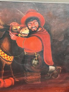 20th Century Fine Art Martin Trainer Oil Painting Of Matador With Mule Circa - 20th Century Composition - Oil On Board Listing Description Charming Stylised Artwork Of Matador And Mule By Known Artist MARTIN TRAINER. The Central Focal Point of The Painting Depicts A Smiling Matador Wearing Red Hat And Cape. Kneels On Wooden Step Adjusting His Mules Bridal. A Bottle of Liquor Hangs From His Waist Belt. Happy Mule In Riding Tack With Checkered Band Stands Next To His Owner. Eary Backdrop With Auburn Moon Illuminating Buildings In Dark Silhouette. Fine Quality Artwork Painted On Board And Set In Glazed Wood Frame. Dimensions In Inches Height 21" X Width 26"