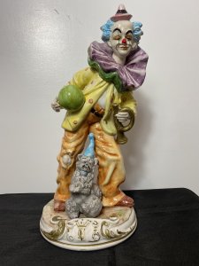 Magnificent Large Capodimonte Bright Glazed Circus Clown Figurine With Dog Companion. Circa - Vintage Composition - Glazed Porcelain Listing Description Large Stylised Hand Painted Circus Clown With Bold Face Paint, Blue Tufted Hair And Pointed Pink Hat. Oversized Double Flounced Neck Ruff Over Vibrant Yellow Spotted Coat. Orange Baggy Trouser With Comical Teared Hole At The Knee. This Magnificent Clown Holds Green Ball And Bugle Horn. A Fellow Dog Companion Sits Poised Upon The Circular Base With Blue Collar And Matching Hat. Wonderful Rare Piece For Collector Of Clowns \ Capodimonte And Circus Memorabilia. Condition - Used Sadly The Top Of The Bugal Has Been Damaged Please See Images. A Few Small Chips To Paint Visible Due To Age And Usage. This Does Not Detract From The Beauty Of The Piece But Is Reflective In The Price. Dimensions In Inches Height 20" Width 9" Depth 10"