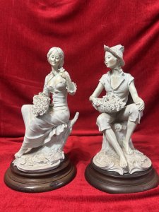 Pair Of Traditional Italianate Sitting Male/Female Capodimonte Style Figurines On Wood Plinths Circa - 1980 Composition - Porcelain on Wood Plinth Listing Description Wonderful Perfect Pair Of Italian Capodimonte Style Figurines. Female Sitting On Tree Stump With Floral Basket, Holds Rose In left Hand. Male Seated On Tree Stump Wears Straw Hat Holding Fruit Basket. Both Signed On Base By Artist A Berni And ADT ITALY With Capodimonte Style Ink Mark. Set Upon Polish Wood Base Plinths. Dimensions In Cms Male Height 32cm X Width 16cm X Depth 20cm X Base Diam 18cm Female Height 31.5cm X Width 16cm X Depth 14cm x Base Diam 18cm