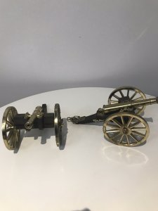 A Pair Of Vintage Military Gun Cannons In The Napoleonic Style Solid Guilt Bronze Metal Barrels With Spoke Wheels And Towing Hooks To Be Pulled By Horses At Battle Exceptional Detail With Hardwood Gun Carriage Quality Replica Guns Heavy And Handmade By Craftsman In England Collectors Items Dimensions In Inches Length 7 1/4 “ Wheels Height 4” Gun Barrel Length 4 3/4