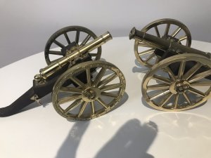 A Pair Of Vintage Military Gun Cannons In The Napoleonic Style Solid Guilt Bronze Metal Barrels With Spoke Wheels And Towing Hooks To Be Pulled By Horses At Battle Exceptional Detail With Hardwood Gun Carriage Quality Replica Guns Heavy And Handmade By Craftsman In England Collectors Items Dimensions In Inches Length 7 1/4 “ Wheels Height 4” Gun Barrel Length 4 3/4