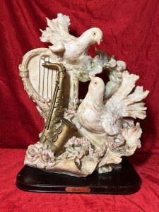 Large Italianate Romantic Turtle Doves & Instrumental Showpiece On Wood Plinth Signed Circa - 20th Century Composition - Resin Listing Description Wonderful Large Elaborate Italianate Centrepiece Depicting Pair Of Turtle Doves Entwined Amongst Musical Instruments And Vines Of Pink Roses And Pale Blue Orchids. The Turtle Doves Are Posed With One Nestled On Top Of A Strung Harp Gazing Downward At The Other Perched Upon A Whimsical Books Of Literature Next To Gilt Saxophone. An Abundance Of Flowers Flow In A Ornamental Bouquet From The Base Of The Sculpture Entwining All Elements. A Head Of Winged Cherub Is Visible Under The Top Dove On Both Front And Back Elevations. Fine Quality Hand Painted Sculpture Showpiece Can Be Admired From All Elevations. Set Upon Polished Mahogany Plinth With Front Plaque Reads 'Huda Italy' & Stamped On Back Elevation. Provenance Actual Showpiece Used As Decorative Prop In The Film 'Victoria'. Now Part of Lord Hill Museum Private Collection. For Further Information Regarding Any Of Our Stock Please Call 07376 618513 Thank-You Dimensions In Inches Height 20.5" Width 17" Depth 9"