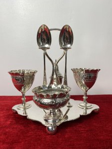Antique Elegant Egg Cruet Breakfast Set In Christopher Dresser Style. Circa - 1870/75 Composition- EPNS Silver Plate Beautiful Antique Original Breakfast Cruet Set Which Includes Salt Bowl, Pepper Shaker, Two Egg Cups, Two Spoons And Ornate Stand. Delicate Pieces With Scalloped Edges, Ornate Repoussé Work Of Vine Leaves And Scrolls Set Upon Elegant Diamond Clover Shaped Base With Handle, Spoon Holders And Bun Feet. Hallmarked And Stamped. Fabulous Quality Set In Christopher Dresser Aesthetic Movement Style. Dimensions In Inches Height 7” Width 6 1/4” Depth