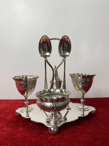 Antique Elegant Egg Cruet Breakfast Set In Christopher Dresser Style. Circa - 1870/75 Composition- EPNS Silver Plate Beautiful Antique Original Breakfast Cruet Set Which Includes Salt Bowl, Pepper Shaker, Two Egg Cups, Two Spoons And Ornate Stand. Delicate Pieces With Scalloped Edges, Ornate Repoussé Work Of Vine Leaves And Scrolls Set Upon Elegant Diamond Clover Shaped Base With Handle, Spoon Holders And Bun Feet. Hallmarked And Stamped. Fabulous Quality Set In Christopher Dresser Aesthetic Movement Style. Dimensions In Inches Height 7” Width 6 1/4” Depth