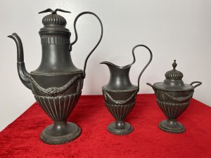 Fine Antique 18th Century KONIGSBERG Germany 3Pc Pewter Coffee Service Circa - 18th Century Composition - Pewter Elegant Fine Quality 3 Piece Pewter Coffee Service By German Makers KONIGSBERG. 3 Piece Set Comprised Of A Large Coffee Pot, Milk Jug And Sugar Bowl. The Tall Coffee Pot Has A Ornemental Dome Topped Lid, Decorated With A Soaring Eagle. The Tapered Neck Leads Into A Urn Shaped Body Decorated With Floral Garlands, Segmented Relief Pattern, Eloquent Curved Carry Handle And Elaborate Spout. The Coffee Pot Stands Upon A Circular Base With Ball And Dart Decoration And Scalloped Edge. The Milk Jug Has Matching Curved Carry Handle, Elevated Pouring Spout, With Swag Of Garlands Around Body & Set On Matching Circular Egg And Dart Base. The Lidded Sugar Bowl Has A Removable Top With Elaborate Dome And Pinnacle, Matching Garland Swags Around The Body With Curved Carry Handle And Pouring Spout. Set Upon Circular Egg And Dart Decorated Stand. Fine Quality Antique Set With All Pieces Stamped Underneath KONIGSBERG Makers Mark. Dimensions In Inches Coffee Pot Height 12" X Width 8.5"X Depth 5" Milk Jug Height 8 1/4" X Width 5 1/4" X Depth 4" Sugar Bowl Height 7.5" X Width 5.5" X Depth 4.5"