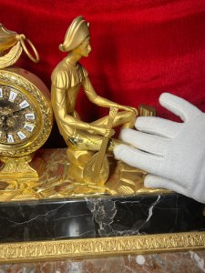 Italian Empire Figural Salon Clock With Posed Court Jester Holding Loot Circa -1950 Composition - Gilt Bronze/ Marble Listing Description A Fine Italian Gilt Bronze Timepiece Showcasing Clock Set Upon Column Mount, With Circular Bezel Face. Enamel Plaque Roman Numeral Dial With Fleur De Lys Decoration And Delicate Folate Hands. Large Ornamental Handled Urn Top Pinnacle And Unusual Sweeping Feather Plume. A Court Jester In Harlequin Costume Sits Against The Clock, Holding Loot Instrument Surrounded By Fallen Column Pillars. Figural Display Is Mounted Upon Black Marble Pediment With Gilt Bronze Frieze. Wonderful Timepiece With Rare Subject. Condition Report Signs Of Tarnishing To Gilt Work Due To Age And Usage. Dimensions In Inches Height 15" X Width 19" X Depth 8" PLEASE NOTE This Is A Very HEAVY ITEM. Due To This Heavy Nature Of This Clock, Delivery Will Be By Hand By Our Curator , Personal Collection By Buyer Or Collection By Specialist Courier Organised By The Buyer. For Further Information Or Enquiries Please Call The Curator On 07707 488566