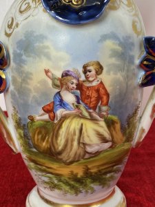 Sevres Style Romantic Porcelain Vase With Branch Handles And Flora Decorations. Circa ~1880 Leaf Adorned Vase Top In Asymmetric Pattern Heavily Gilt With Green And Blue Coloration. Heart Shaped Branch Like Handles With Three Floral Plaque Decorations. Central Romantic Panel Of Loving Couple In 18Th Century Clothing Reclining In Delicate Shadowed Landscape. Delicate Pastel Hues Complemented With Vibrant Green And Royal Blue. Makers Mark No 71 P&A Embossed On Base. Condition- Antique Used Perfect Condition No Damage. Wear To Gilt Work Decoration Conducive To Age And Usage. Dimensions In Inches Height 12” Width 7”