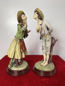 Pair Of Charming Porcelain Capodimonte Kissing Statuettes. Vintage Male And Female Pair Of Kissing Statuettes. The Lady Holds A Basket Of Oranges And Gracefully Leans In The Kiss The Male. The Male Figurine Holds A Posy Behind His Back And Leans In The Kiss His Fair Maiden. Beautiful Details, Hand Painted And Signed On The Bases. Standing On Mahogany Circular Plinths. Condition- Lovely Used Slight Damage To Finger Of Lady Otherwise Perfect Condition Dimensions In Inches Height 14 3/4” Width 5.5” Depth 5.5”