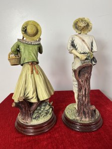Pair Of Charming Porcelain Capodimonte Kissing Statuettes. Vintage Male And Female Pair Of Kissing Statuettes. The Lady Holds A Basket Of Oranges And Gracefully Leans In The Kiss The Male. The Male Figurine Holds A Posy Behind His Back And Leans In The Kiss His Fair Maiden. Beautiful Details, Hand Painted And Signed On The Bases. Standing On Mahogany Circular Plinths. Condition- Lovely Used Slight Damage To Finger Of Lady Otherwise Perfect Condition Dimensions In Inches Height 14 3/4” Width 5.5” Depth 5.5”