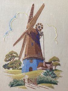 Stunning Vintage Windmill Hand Embroidered Silk Artwork Set In Glazed Frame. Circa- Vintage 1890 Composition- Hand Embroidered Silk Thread Artwork Condition - Lovely Vintage Original Beautifully Quaint And Detailed Composition Of A Large Windmill Set In Rich Flora & Forma Landscape. Rich Blue Rendered Windmill With Half Wooden Cladding Leading Up To Giant Turbines. Picturesque Details Of Wooden Door And Small Windows With Lovely Cottage Style Picket Fence & Planted Garden. Stunning Richly Coloured Composition Created Out Of Many Embroidery Stitches Which Include Straight / Back Stitch, French Knots And Running Stitches. Beautiful Example Of A Hand Embroidered Artwork Set In Glazed Wooden Frame. Dimensions In Inches Height 21.5” Width 17.5”