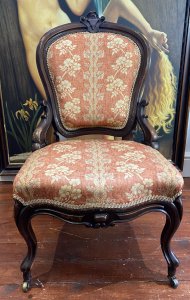Ladies French Empire Sewing Chair With Elegant Floral Upholstery. Antique Sewing Chair With Carved Solid Walnut Frame. Padded Harp Shaped Back Rest With Cartouche Crest Top Pinnacle And Highly Elaborate Scroll Supports. Sprung Shaped Seat. Stands Upon Cabriole Scrolled Front And Splayed Back Legs Over Solid Brass Castors For Ease Of Movement. Exceptional Example Of Genuine Antique Chair Dated 1870 Sewing Chair. Stunning Original Patina And Condition With Wear Marks On The Woodwork Due To Age. Upholstery In Pristine Condition. Delicate Floral Upholstery In Rosey Peach Colour With Symmetrical Floral Spray Pattern. Edged In Light Gold Gimp Braid. Craftsman Made. Exceptional Comfort. Stunning Highly Decorative Ladies Chair For Boudoir Or Lounge. Dimensions In Inches Back Height 38.5” Width 22” Depth 21” Seat Height 16”