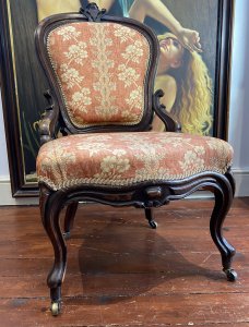Ladies French Empire Sewing Chair With Elegant Floral Upholstery. Antique Sewing Chair With Carved Solid Walnut Frame. Padded Harp Shaped Back Rest With Cartouche Crest Top Pinnacle And Highly Elaborate Scroll Supports. Sprung Shaped Seat. Stands Upon Cabriole Scrolled Front And Splayed Back Legs Over Solid Brass Castors For Ease Of Movement. Exceptional Example Of Genuine Antique Chair Dated 1870 Sewing Chair. Stunning Original Patina And Condition With Wear Marks On The Woodwork Due To Age. Upholstery In Pristine Condition. Delicate Floral Upholstery In Rosey Peach Colour With Symmetrical Floral Spray Pattern. Edged In Light Gold Gimp Braid. Craftsman Made. Exceptional Comfort. Stunning Highly Decorative Ladies Chair For Boudoir Or Lounge. Dimensions In Inches Back Height 38.5” Width 22” Depth 21” Seat Height 16”