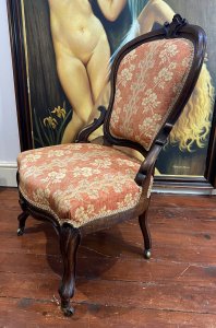 Ladies French Empire Sewing Chair With Elegant Floral Upholstery. Antique Sewing Chair With Carved Solid Walnut Frame. Padded Harp Shaped Back Rest With Cartouche Crest Top Pinnacle And Highly Elaborate Scroll Supports. Sprung Shaped Seat. Stands Upon Cabriole Scrolled Front And Splayed Back Legs Over Solid Brass Castors For Ease Of Movement. Exceptional Example Of Genuine Antique Chair Dated 1870 Sewing Chair. Stunning Original Patina And Condition With Wear Marks On The Woodwork Due To Age. Upholstery In Pristine Condition. Delicate Floral Upholstery In Rosey Peach Colour With Symmetrical Floral Spray Pattern. Edged In Light Gold Gimp Braid. Craftsman Made. Exceptional Comfort. Stunning Highly Decorative Ladies Chair For Boudoir Or Lounge. Dimensions In Inches Back Height 38.5” Width 22” Depth 21” Seat Height 16”