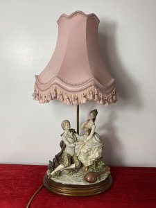 Large Italian Masterpiece ‘The Lovers Proposal’ Capodimonte Figurine Lamp. Circa - Vintage 1970s Composition- Porcelain Figurine With Light Fixture Maker - Capodimonte Breathtakingly Beautiful Capodimonte Figurine Lamp Depicting Italian Renaissance Nobility Titled ‘Young Lovers Proposal’. Finest Quality Craftsmanship In Hard Paste Porcelain Signed By Artist And Numbered (On Back). Sitting Male And Swooning Female Perched On Ornamental Chair. Dressed In Garments Of Nobility With Fine Silks And Laces Delicately Recreated In Porcelain. With Powdered Wigs, Intricate Facial Details And Expressions. Charming Ukulele Instrument Lies Face Down Upon The Floor Laden With Delicate Flowers. Ornamental Elaborate Pink Shade With Pink Fringing. Stands Upon Wooden Base With Brass Feet. Fitted With U.K. 3 Prong Plug. This Truly Stunning Piece Tells A Truely Romantic Story. This Elegant Lamp Would Be Perfect For A Boudoir, Lounge Or Living Area A Real Talking Point. Condition- Perfect Figurine No Damage. Light Working Dimensions In Inches Overall Height 27” Figurine Height 13” Figurine Width 10.5” Figurine Depth 6.5” Base Width11 1/4” Base Depth 9.5”