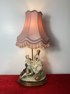 Large Italian Masterpiece ‘The Lovers Proposal’ Capodimonte Figurine Lamp. Circa - Vintage 1970s Composition- Porcelain Figurine With Light Fixture Maker - Capodimonte Breathtakingly Beautiful Capodimonte Figurine Lamp Depicting Italian Renaissance Nobility Titled ‘Young Lovers Proposal’. Finest Quality Craftsmanship In Hard Paste Porcelain Signed By Artist And Numbered (On Back). Sitting Male And Swooning Female Perched On Ornamental Chair. Dressed In Garments Of Nobility With Fine Silks And Laces Delicately Recreated In Porcelain. With Powdered Wigs, Intricate Facial Details And Expressions. Charming Ukulele Instrument Lies Face Down Upon The Floor Laden With Delicate Flowers. Ornamental Elaborate Pink Shade With Pink Fringing. Stands Upon Wooden Base With Brass Feet. Fitted With U.K. 3 Prong Plug. This Truly Stunning Piece Tells A Truely Romantic Story. This Elegant Lamp Would Be Perfect For A Boudoir, Lounge Or Living Area A Real Talking Point. Condition- Perfect Figurine No Damage. Light Working Dimensions In Inches Overall Height 27” Figurine Height 13” Figurine Width 10.5” Figurine Depth 6.5” Base Width11 1/4” Base Depth 9.5”