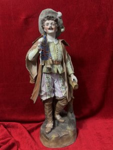 Parian Hand Painted Bisque Cavalier Figurine Holding Britannia Flag Circa - 1890 Composition - Hard Paste Porcelain Listing Description Exceptional Parian Figurine Of Gentleman Cavalier Extravagantly Dressed Hat With Feather Plumes, Lemon Belted Front Buttoned Shirt, Pink Floral Pantaloons, Cape And Brown Leather Knee High Boots. Cavalier Holds British Ensign Flag With Gilt Tassels In Right Hand. Condition - Excellent Antique Figurine Showing Age Cracks In Porcelain. Dimensions In Cms Height 52cm X Width 20cm X Depth 18cm Base 17cm SQ For Further Information Please Call The Museum Curator On 07707 488566 Thank-you.