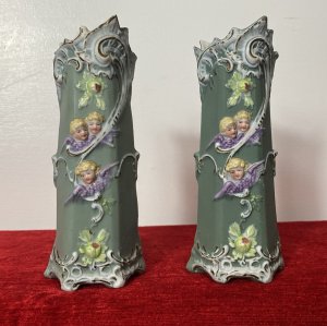 Pair Of Elaborate French Parian Ware 'Trio Of Winged Putti' Posey Vases Circa - Composition - Bisque Porcelain Colour - Green Listing Description Pair Of Hexagonal Cylinder Vases In Hard Paste Porcelain With Elaborated Decoration Of Three Winged Cherubs With Only Faces And Wings Visible. Putti With Vibrant Blonde Curled Hair, Tonal Skin With Delicate Facial Features And Purple Wings. A Detailed Floral Relief Pattern With Thistles & Hand Painted Gilt Work On Around Neck And Base Of Vases. Numbered On Bases Condition - Antique Used Minor Chip On The Neck Of One Vase Conducive To Age. Please See Images. For Further Images Or Assistance Please Call 07376618513 Dimensions in Inches Height Width Depth