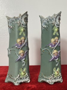 Pair Of Elaborate French Parian Ware 'Trio Of Winged Putti' Posey Vases Circa - Composition - Bisque Porcelain Colour - Green Listing Description Pair Of Hexagonal Cylinder Vases In Hard Paste Porcelain With Elaborated Decoration Of Three Winged Cherubs With Only Faces And Wings Visible. Putti With Vibrant Blonde Curled Hair, Tonal Skin With Delicate Facial Features And Purple Wings. A Detailed Floral Relief Pattern With Thistles & Hand Painted Gilt Work On Around Neck And Base Of Vases. Numbered On Bases Condition - Antique Used Minor Chip On The Neck Of One Vase Conducive To Age. Please See Images. For Further Images Or Assistance Please Call 07376618513 Dimensions in Inches Height Width Depth