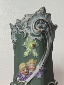 Pair Of Elaborate French Parian Ware 'Trio Of Winged Putti' Posey Vases Circa - Composition - Bisque Porcelain Colour - Green Listing Description Pair Of Hexagonal Cylinder Vases In Hard Paste Porcelain With Elaborated Decoration Of Three Winged Cherubs With Only Faces And Wings Visible. Putti With Vibrant Blonde Curled Hair, Tonal Skin With Delicate Facial Features And Purple Wings. A Detailed Floral Relief Pattern With Thistles & Hand Painted Gilt Work On Around Neck And Base Of Vases. Numbered On Bases Condition - Antique Used Minor Chip On The Neck Of One Vase Conducive To Age. Please See Images. For Further Images Or Assistance Please Call 07376618513 Dimensions in Inches Height Width Depth