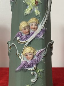 Pair Of Elaborate French Parian Ware 'Trio Of Winged Putti' Posey Vases Circa - Composition - Bisque Porcelain Colour - Green Listing Description Pair Of Hexagonal Cylinder Vases In Hard Paste Porcelain With Elaborated Decoration Of Three Winged Cherubs With Only Faces And Wings Visible. Putti With Vibrant Blonde Curled Hair, Tonal Skin With Delicate Facial Features And Purple Wings. A Detailed Floral Relief Pattern With Thistles & Hand Painted Gilt Work On Around Neck And Base Of Vases. Numbered On Bases Condition - Antique Used Minor Chip On The Neck Of One Vase Conducive To Age. Please See Images. For Further Images Or Assistance Please Call 07376618513 Dimensions in Inches Height Width Depth