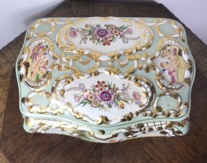 Stunning Object Of Virtue Marie Antoinette Sevres Style Porcelain Trinket Casket. French Origin Bombay Shaped Porcelain Jewellery/Trinket Casket Profusely Hand Painted With Panels Of Putti With Flora And Forna Painted In Stunning Cartouches Bronze Hinged Lid With Bronze Closing Clasp In Leaf Work With Reposed Cherubs In Landscape Stands Upon Four Shaped Cabriole Legs Heavily Gilded Grand Tour Quality Specimen Delivery By Our Butler To Your Door UK Same Day If Desired. Provenance Purchased From Chateau In Paris From Baron Dupree 1973 Dimensions In Inches Height 9.5” Width 13.5” Depth 11”