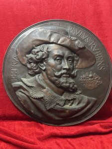 Circa - 19th Century Composition - Beaten Copper Large Copper Wall Plaque Depicting Flemish Baroque Painter Sir Peter Paul Ruben’s Classical Relief Portrait Showing Artist Peter Paul Ruben’s At The Tome The Plaque Was Created Wearing A Large Tassel Hat And Oversized Lace Collar. The Artist Gazes To The Right. A Decorative Coat Of Arms Placed Near The Face And Artist Ruben’s Name In Latin Scripture Inscribed Around The Top Edge. Stunning Craftsmanship A Wonderful Historic Showpiece. Dimensions In Inches Height 25.5” X Depth From Wall 2”