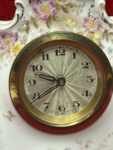 Antique German Dresden mantel clock, circa 1880, crafted from white hard-paste porcelain and decorated with spring floral bouquets and gilt border detailing. Features a machined silver clock face and a seven-day movement. Numbered on the base. Dimensions: 16 cm high × 13 cm wide × 6.5 cm deep. Clock face diameter: 6.5 cm.